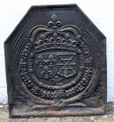 A cast iron fire back decorated in relief with a coat of arms surrounded by ribbons.