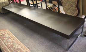 A contemporary unusually long coffee table. The stained wooden top raised upon chrome supports.