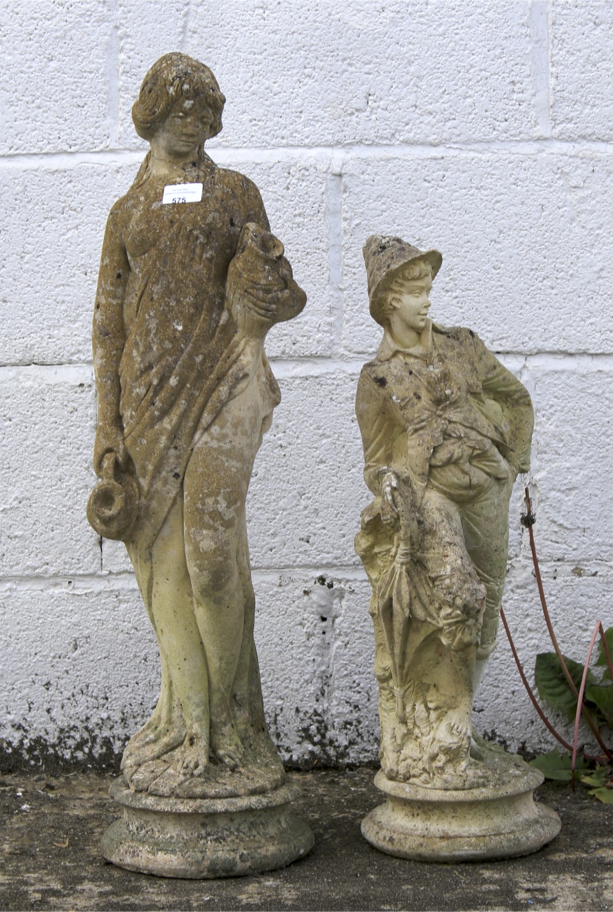 Two composite stone garden figures in the form of a girl with a vase and a boy with a parasol.