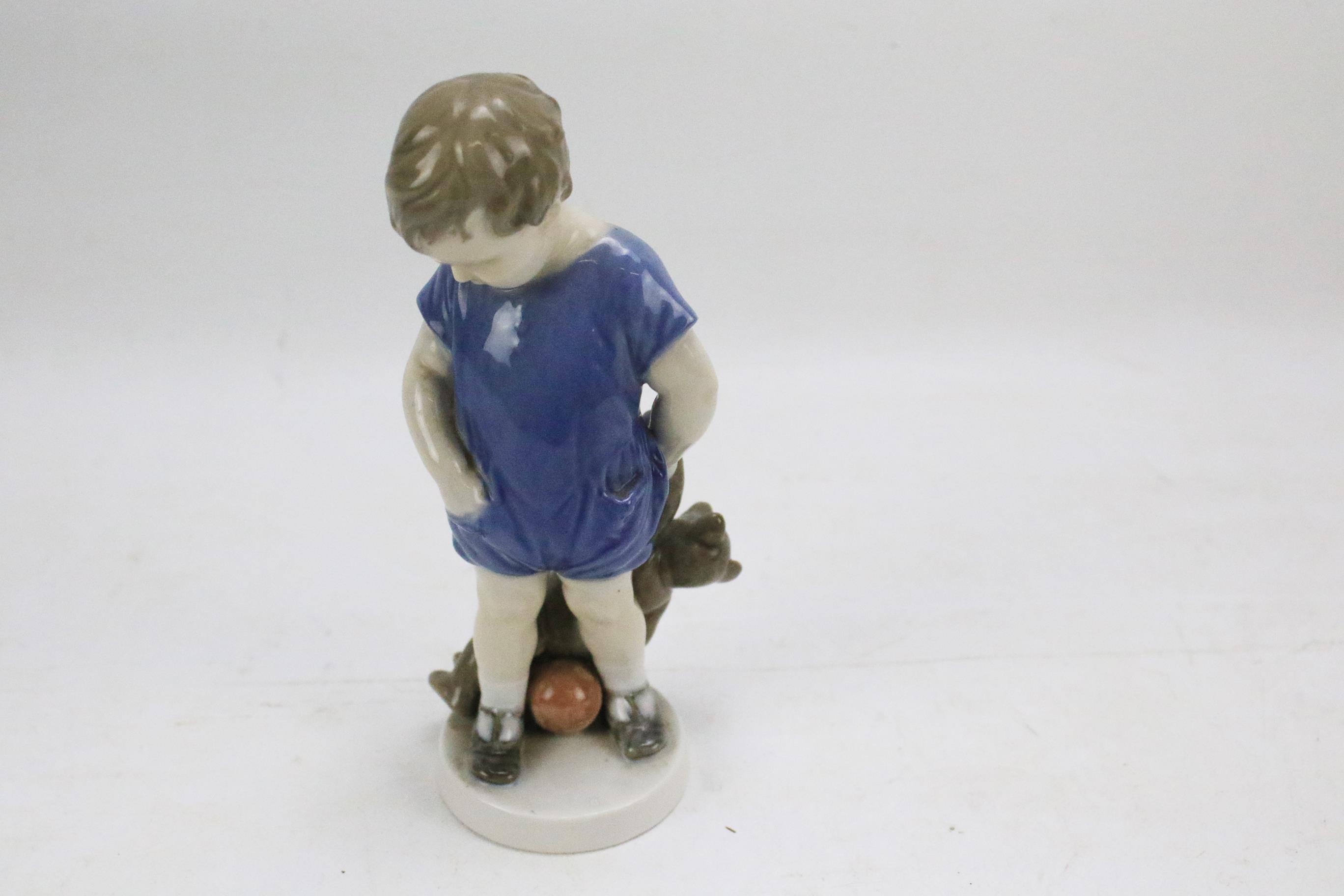 A Royal Copenhagen porcelain figure of a child holding a teddy bear.