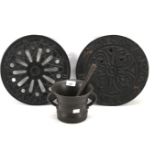 Two cast metal drain covers and a mortar and pestle.