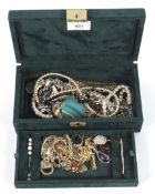 A green velvet box containing an assortment of vintage jewellery.