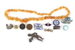 A collection of enamelled pin badges and a simulated amber necklace.