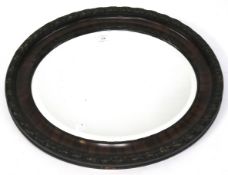 A bevelled edge wall mirror. Of oval form with a mahogany veneered frame, diameter 64cm.