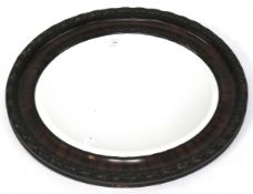 A bevelled edge wall mirror. Of oval form with a mahogany veneered frame, diam 64cm.