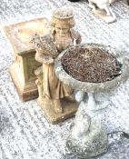 A stone figure of a lady carrying a bundle of wheat, on a pedestal base, and a bird bath.