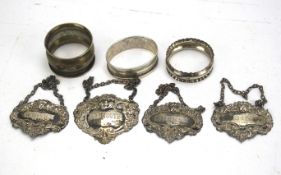 A collection of four silver decanter labels and three silver napkin rings.