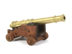 An artillery brass mounted desk top cannon on a wooden carriage.