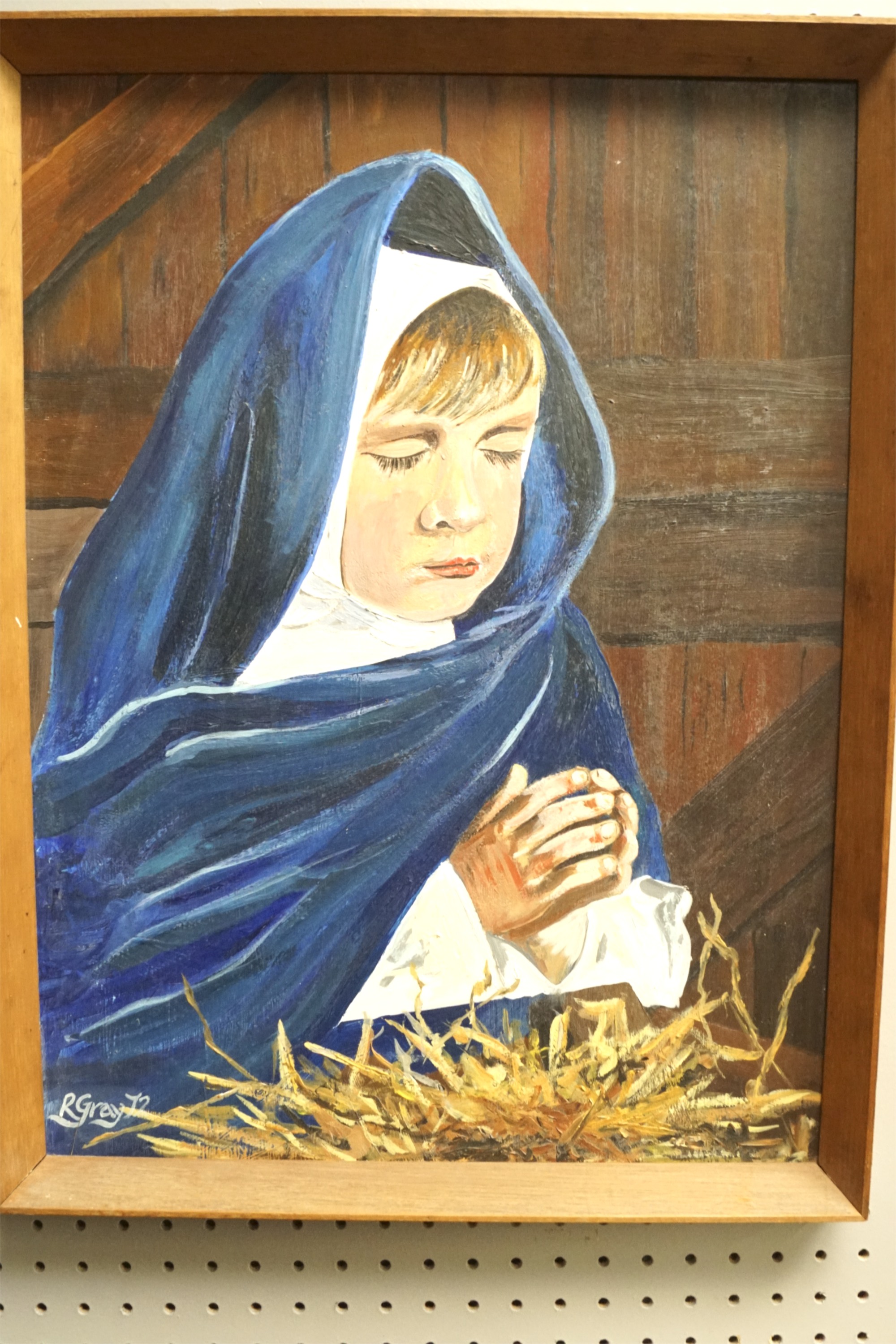 An acrylic on board of a child dressed as the Virgin Mary praying at the manger.