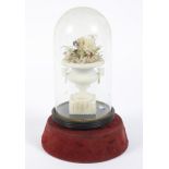 A Victorian carved alabaster urn filled with fabric flowers, under a glass dome.