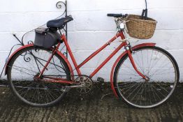 A vintage red painted bicycle with wicket basket to front.