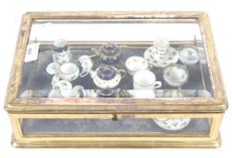 A vintage glazed gilt wooden collectables case with a selection of miniature porcelain items.