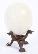 A 20th century carved ostrich egg raised upon a wooden stand.