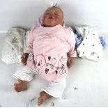A modern, lifelike, heavy baby doll. Wearing baby clothes, depicted asleep.