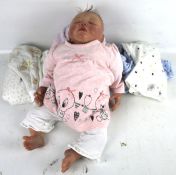 A modern, lifelike, heavy baby doll. Wearing baby clothes, depicted asleep.