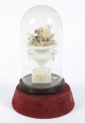 A Victorian carved alabaster urn filled with fabric flowers, under a glass dome.