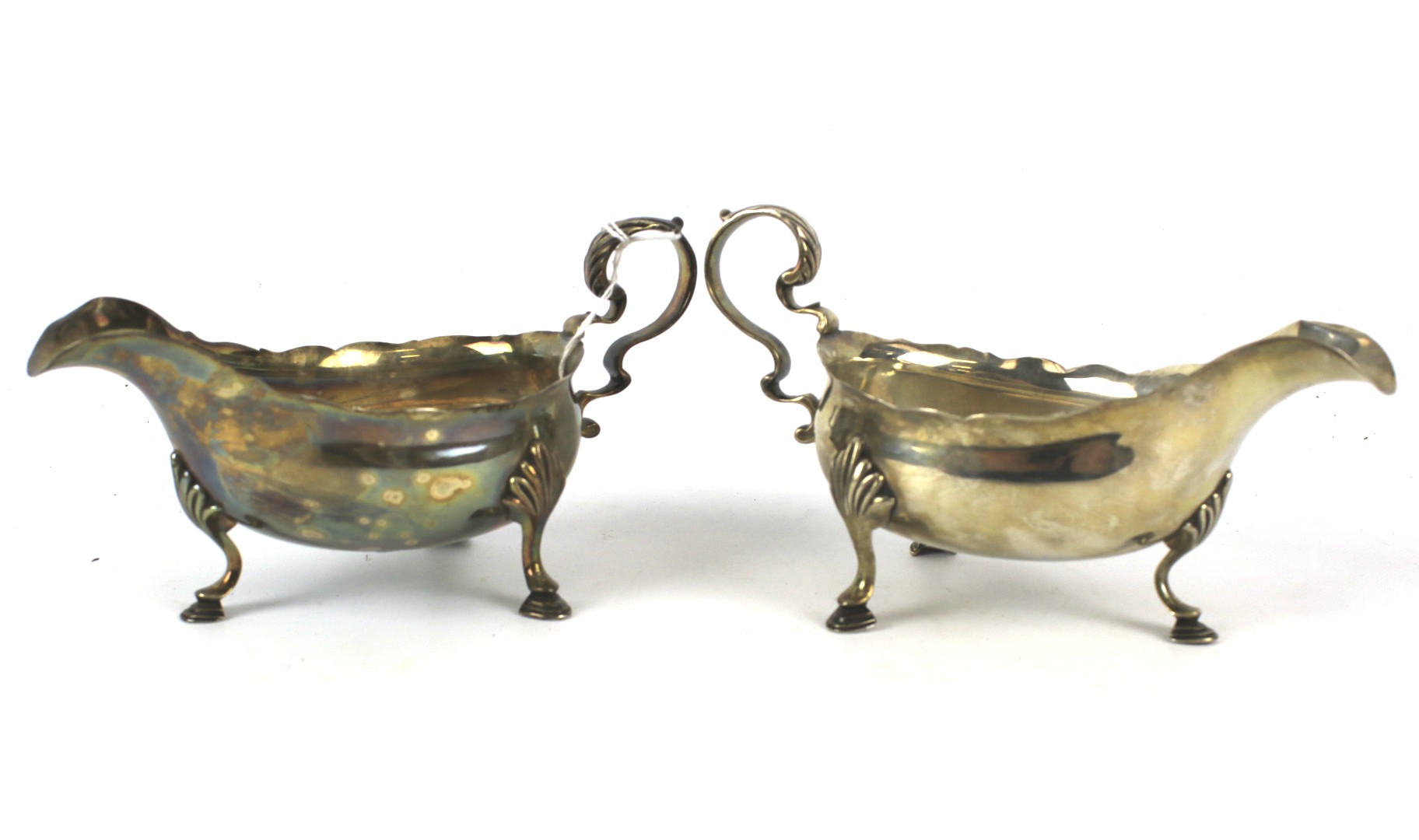 A pair of silver sauce boats with foliate decorated handles. Raised on shell and hoof supports.