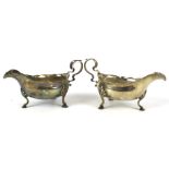 A pair of silver sauce boats with foliate decorated handles. Raised on shell and hoof supports.