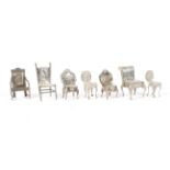 An assortment of seven silver miniature chairs.