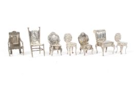 An assortment of seven silver miniature chairs.