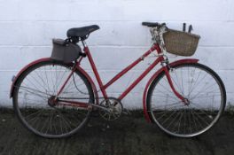 A vintage red painted bicycle with wicket basket to front.