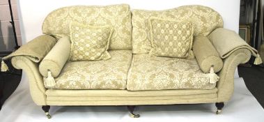 A large cream sofa. With curved back, scrolling arms, raised on turned supports to casters.
