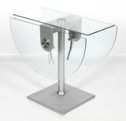 An oval glass drop leaf dining table. Raised on a turned metal column, on a square base, L124.