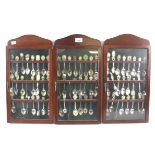 Three glazed wooden display cases containing a collection of souvenir spoons.