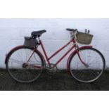 A vintage red painted bicycle with wicker basket to front.