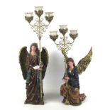Two modern resin figures of angels, each holding three-pronged candelabras.