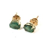 A pair of vintage yellow metal emerald stud earrings. Each oval mixed-cut emerald approx.