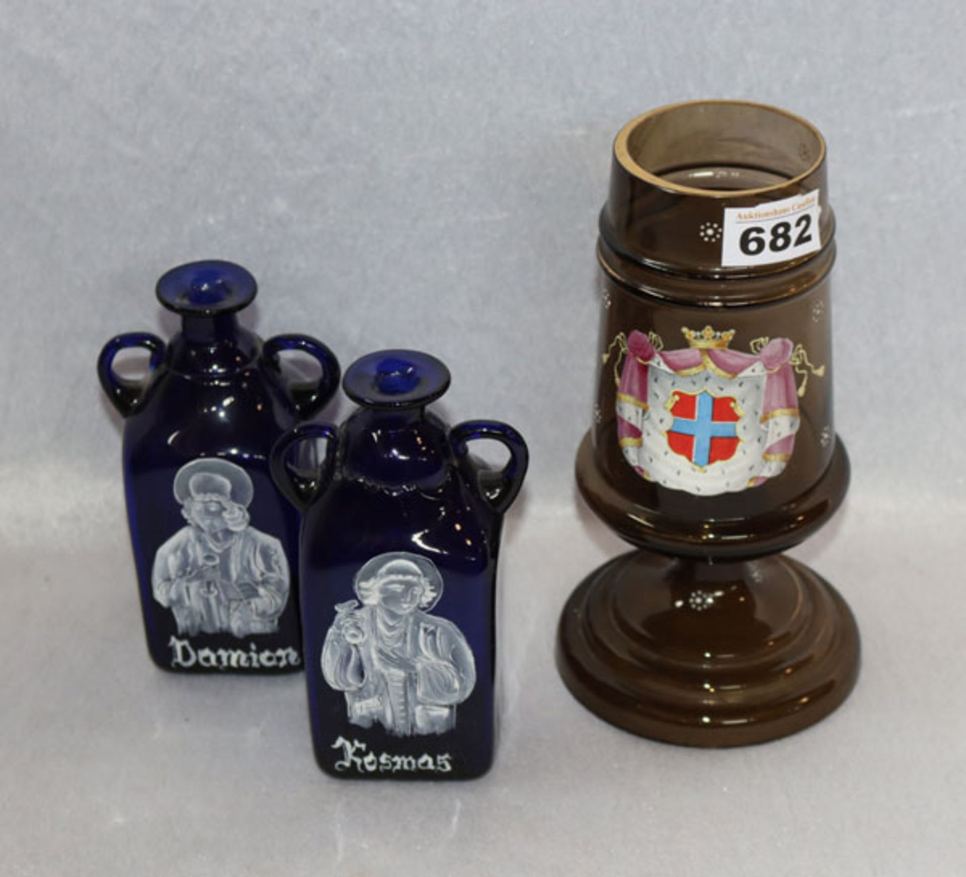 2 blaue Henkelflaschen, weiß bemalt 'Kosmos' und 'Damian', H 17 cm, und braunes Pokalglas mit