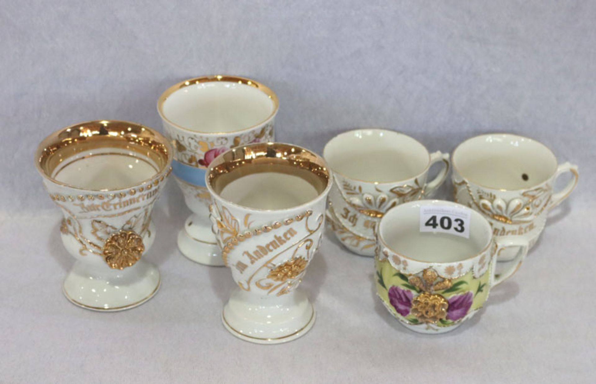 Porzellan-Konvolut: 3 Andenkentassen und 3 Andenken Becher, mit Blumen und Golddekor, teils berieben