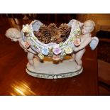 A continental porcelain centrepiece in the form of a floral encrusted basket carried by two cherubs,