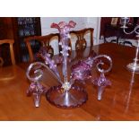 A Victorian cranberry glass epergne, fitted with four flutes and three baskets above a frilled rim