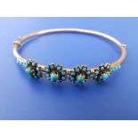 A turquoise set yellow metal bangle, the numerous small stone arranged as four flower heads,