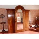 A Victorian mahogany breakfront triple section wardrobe, having high arched central mirror panel