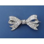 A small diamond millegrain set white metal bow brooch, 0.95" across.