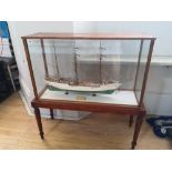 A painted wooden model in glazed display case of the USCGC Barque Eagle, on mahogany stand with