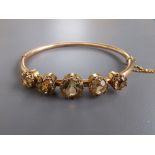 An Edwardian hollow yellow metal bangle, claw set with five yellowish quartz circular cut stones,