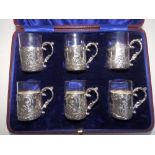 A cased set of six silver liqueur glasses, the plain glass liners in silver sleeves with scrolling