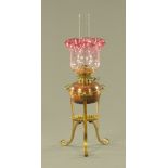 A 19th century brass and copper oil lamp, with cranberry glass shade and reservoir.