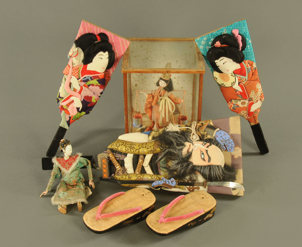 Three Japanese face decorated bats, a cased water carrier figure and a pair of lacquered shoes.