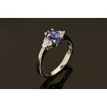 An 18 ct white gold ring, set with an oval cut tanzanite and diamonds to each shoulder. Size M.