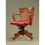 An Edwardian oak revolving desk chair, with slatted back and red leather upholstered seat.