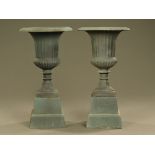 A pair of cast iron Campana shaped garden urns, each raised on a stand, green painted.