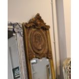 Tall and narrow gilt framed mirror, the upper section decorated with female profile carved panel,