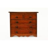 A miniature Victorian chest of drawers, two short and three long with wooden knob handles.