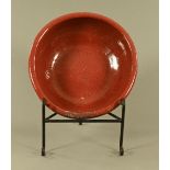 A large circular earthenware bowl, with red glaze and raised on a later wrought iron display stand.