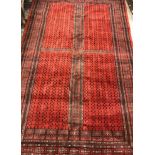 A Bokhara carpet, the central panel split into four, the red ground set with repeating design,